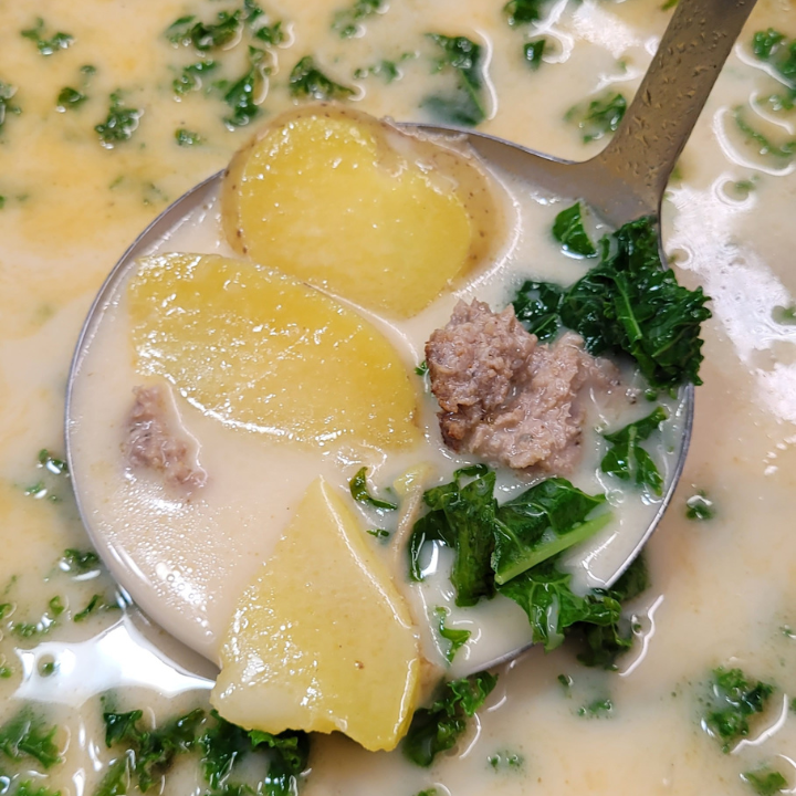 creamy winter soup with sausage, potato, and kale being scooped up with a large ladle